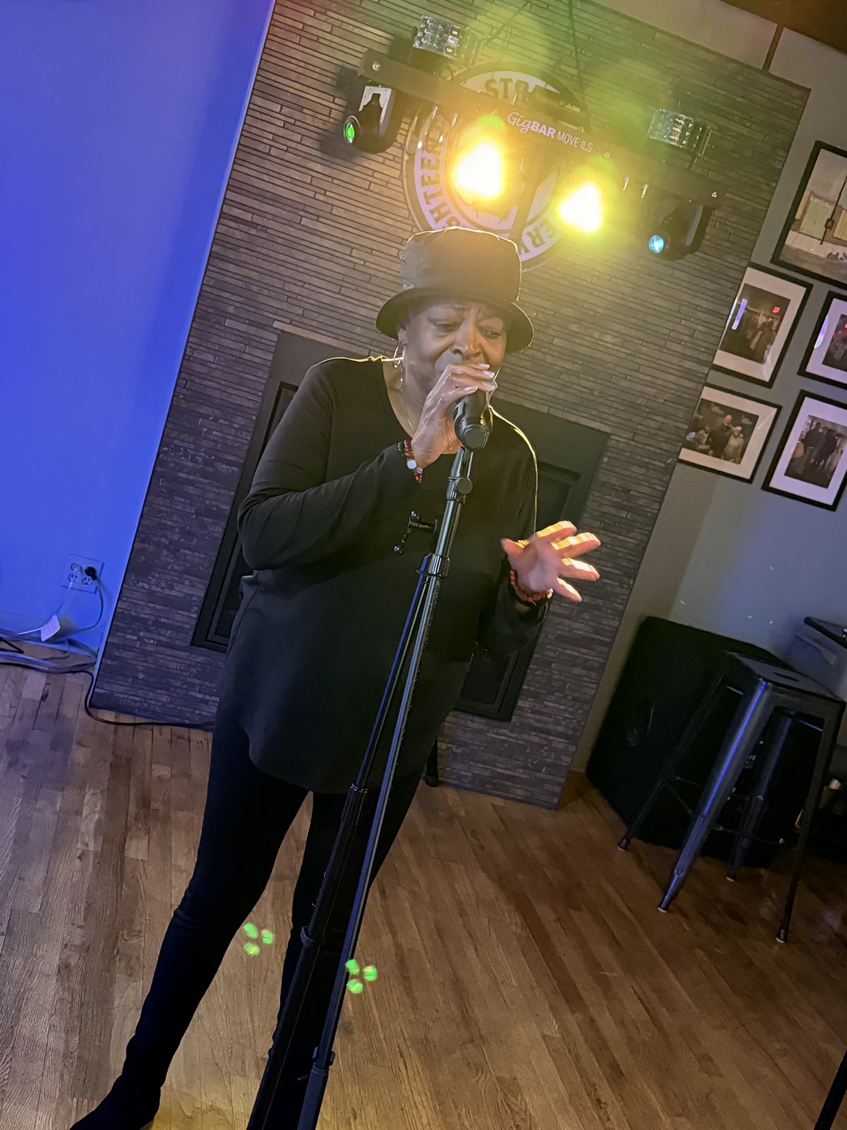 Woman in hat singing at 18th Street Brewery karaoke night with blue stage lighting Gary Indiana